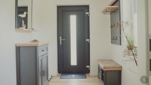 A narrow hallway with a dark door, a small bench, a mirror, and a shelf with decorative items.