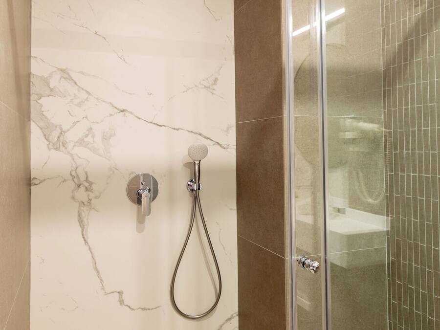 Una ducha moderna con puerta de vidrio, paredes de mármol y suelo de baldosas.
