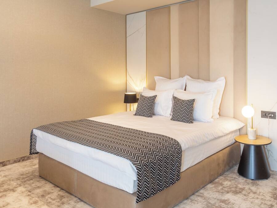 A neatly made bed with a patterned bedspread, a bedside lamp, and a wall-mounted light.