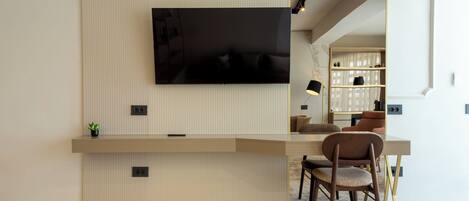 A modern living room with a wooden accent wall, a flat-screen TV mounted above a wooden console, and a seating area with a brown chair and a small table.