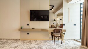 A modern living room with a flat-screen TV mounted on a textured wall, a wooden coffee table, a brown chair, and a large window with curtains. - Lupa By Bueno (Constanta)
