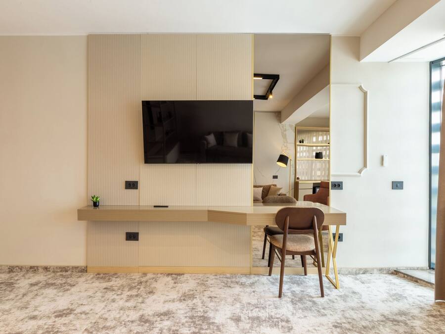 Een moderne woonkamer met een flatscreen televisie bevestigd aan een gestructureerde muur, een houten salontafel, een bruine fauteuil en een groot raam met gordijnen.