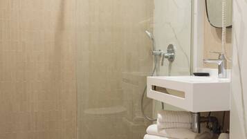 A modern bathroom with a glass-enclosed shower, a white sink with a marble countertop, and a large mirror.
