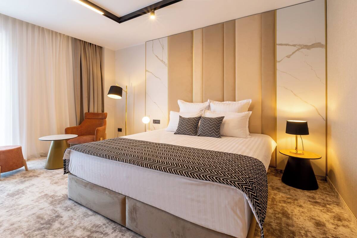 Ein modernes Hotelzimmer mit einem großen Bett, einem Sessel, einem kleinen Tisch und einer Lampe.