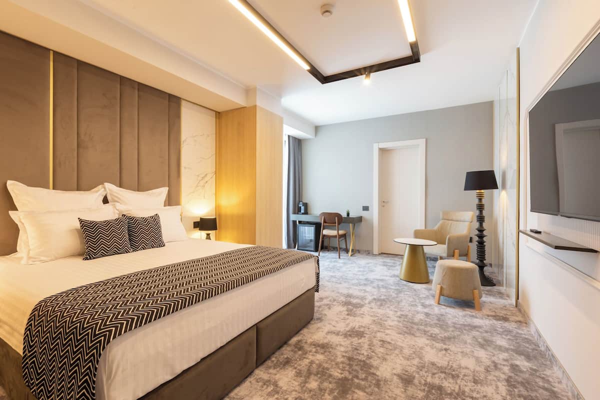 Ein modernes Hotelzimmer mit einem großen Bett, einem Schreibtisch, einem Sessel und einem Fernseher.