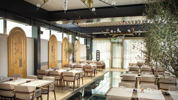 A restaurant with a long dining area, multiple tables, and chairs. There are large windows and a glass partition in the center. - Lupa By Bueno (Constanta)