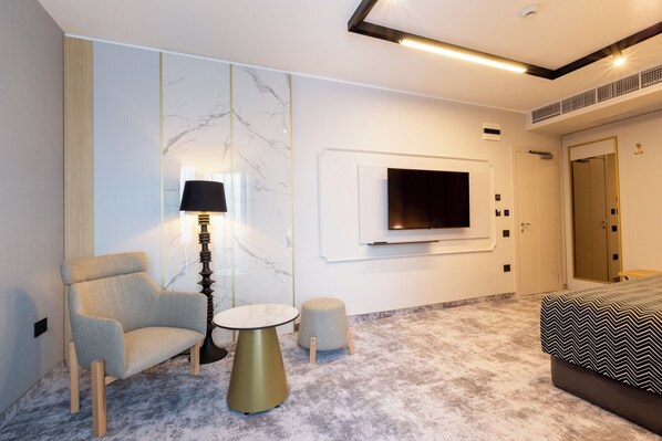 Une chambre d’hôtel moderne avec un mur en marbre, un téléviseur fixé au mur, un lit recouvert d’une couvre-lit à motifs, une chaise, une petite table ronde et une lampe.