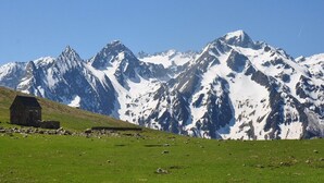 Un paysage de montagne avec un petit bâtiment en pierre situé sur une pente herbeuse.