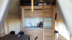Une petite cuisine équipée d’un évier, d’une machine à café et de placards. Une échelle en bois donne accès à une zone de couchage située en mezzanine.