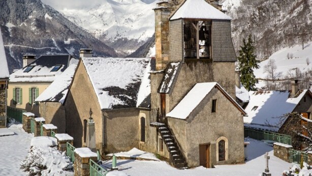 Une église enneigée, dotée d’un clocher, avec une chaîne de montagnes en arrière-plan.