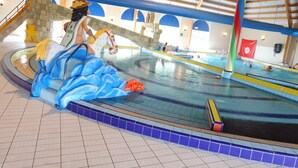 Une piscine intérieure ornée d’une sculpture de dauphin, dotée d’un plafond en bois et d’un drapeau rouge.