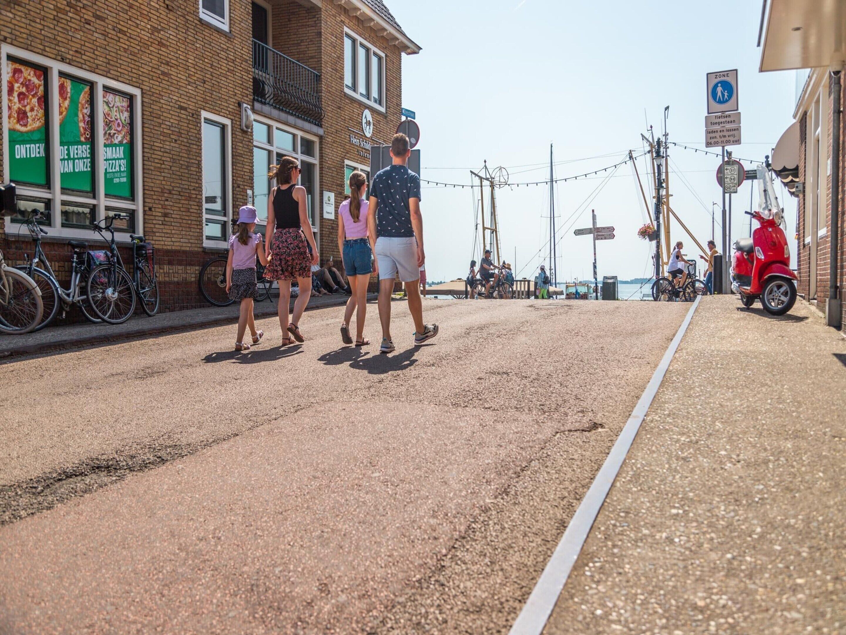 Une rue avec une voie piétonne, des vélos et un scooter rouge garé sur le bord.