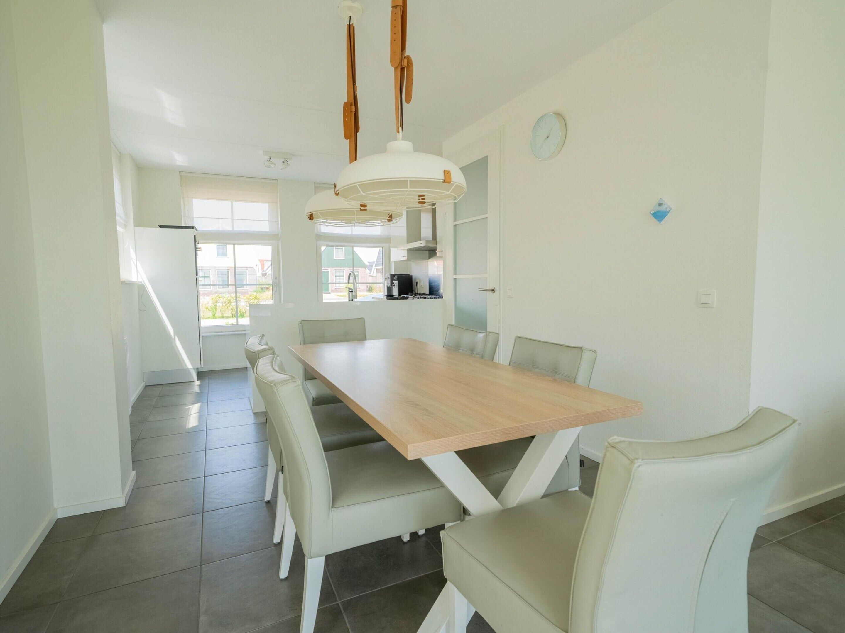 A modern kitchen with a large dining table, white chairs, and pendant lighting.