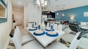A modern dining area with a white table set for four, blue placemats, and a chandelier above.