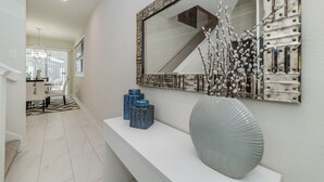 A modern hallway with a white console table, decorative vases, and a large mirror with a metallic frame.
