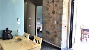 A dining area with a wooden table and chairs, a stone wall, and a view of a bedroom through an open door.