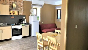 A compact kitchen with a stove, oven, and refrigerator, a wooden dining table with chairs, and a red sofa.