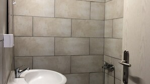 A small bathroom with a white sink, a shower, and a toilet.