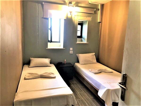 A small, narrow room with two beds, a small table, and a window.