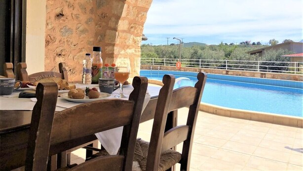 An outdoor dining area with a stone wall, a pool, and a view of the landscape.