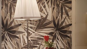 Ein Nachttisch mit Lampe und rotem Blumentopf vor einer Wand mit Blätermuster.