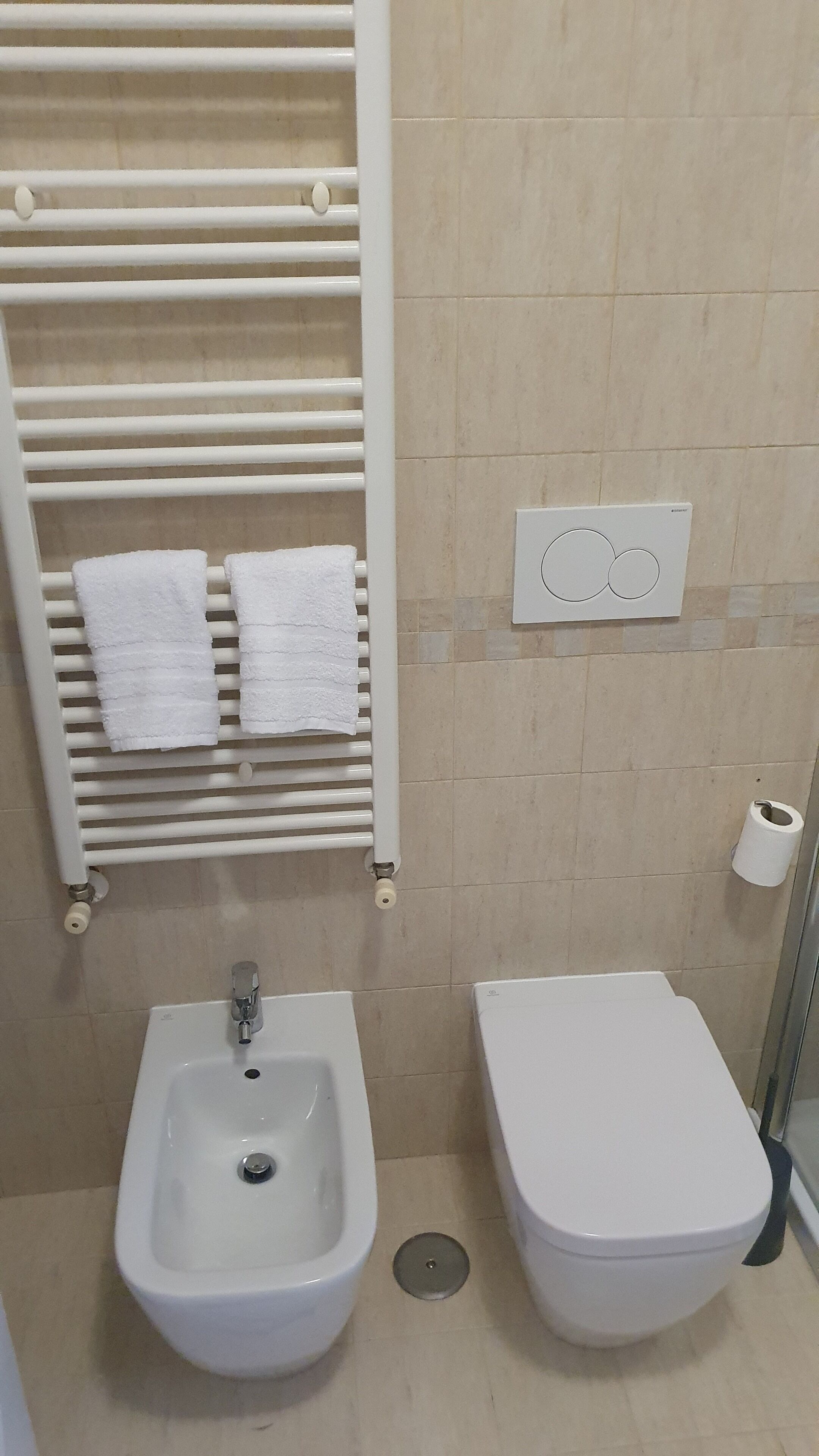 A bathroom with a sink, bidet, and toilet. There are towels hanging on a rack.