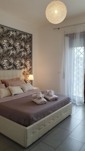 Un dormitorio moderno con una cama grande, un panel decorativo en la pared, una lámpara colgante y vistas a través de cortinas translúcidas.