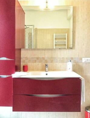 A bathroom with a white sink, a red cabinet, and a mirror above the sink.