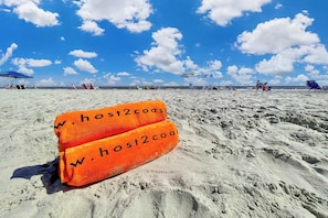 A sandy beach with beach chairs and umbrellas, and two orange towels with 'W.host2coast' text. - Cozy Villa Near Beach Pool & Tennis on Hilton Head (Hilton Head Island)