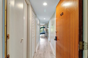 Um corredor com uma porta de madeira, uma parede branca e uma luminária no teto.