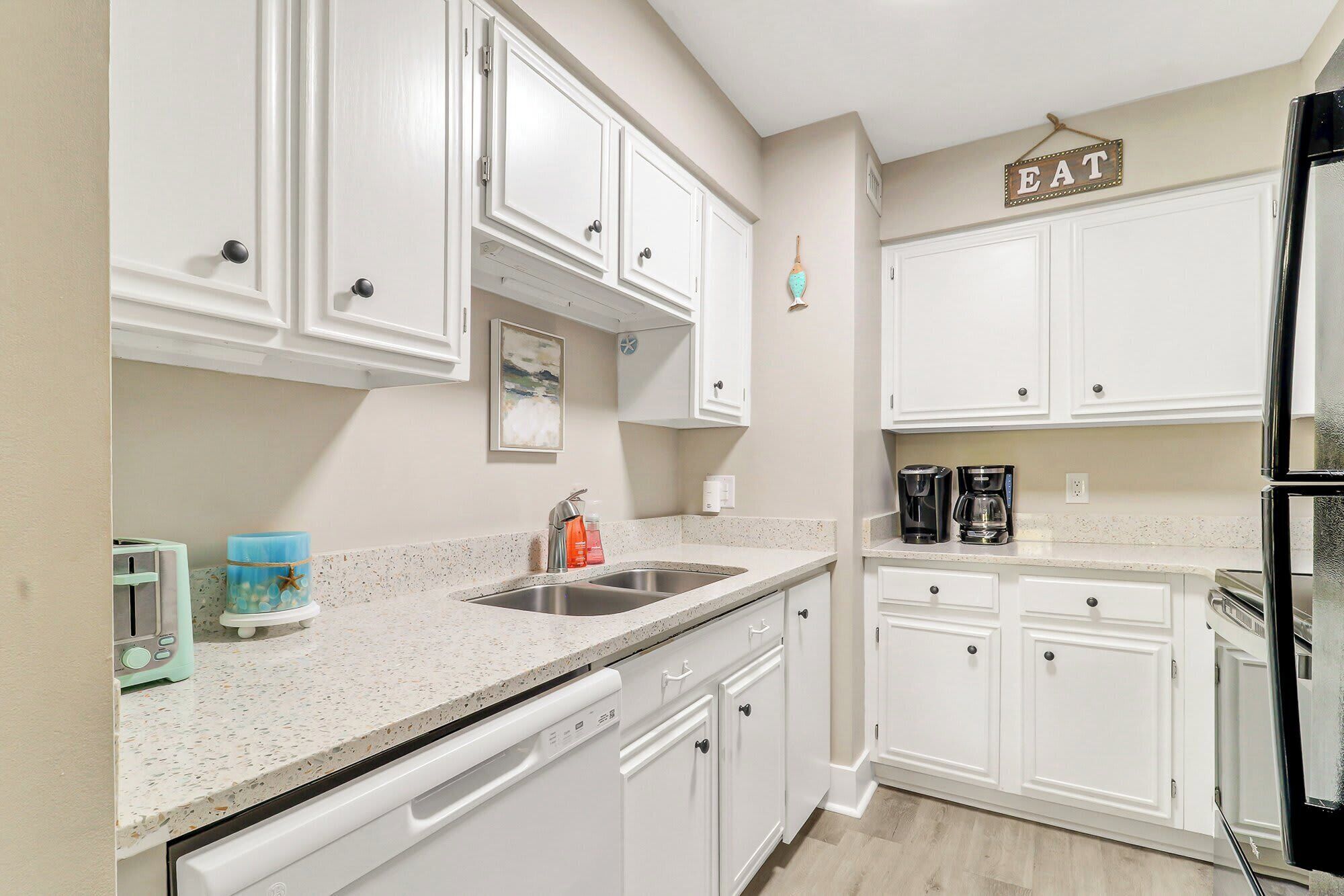 A kitchen with white cabinets, a stainless steel sink, a coffee maker, and a refrigerator.