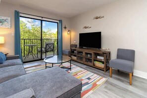 Un salon avec un canapé, une petite table, un téléviseur et un balcon équipé d’une chaise.