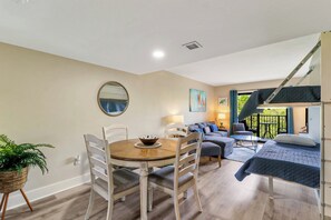 Habitación compacta con una mesa de comedor, sillas, una cama litera y un pequeño rincón de descanso con sofá y mesa.