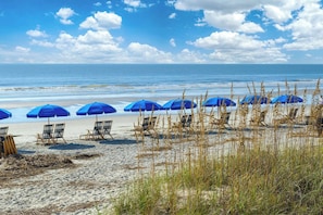 A beach with blue umbrellas and beach chairs.
