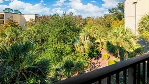Un balcon donnant sur une végétation luxuriante, avec un bâtiment visible au loin.
