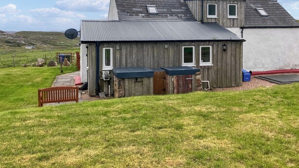 Une maison en bois rustique, dotée d’un toit en pente, d’une petite remise attenante et d’une cour couverte d’herbe.