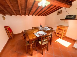 A dining area with a wooden table, chairs, and a small shelf with a radio. - Raffa's Little House (Livorno)
