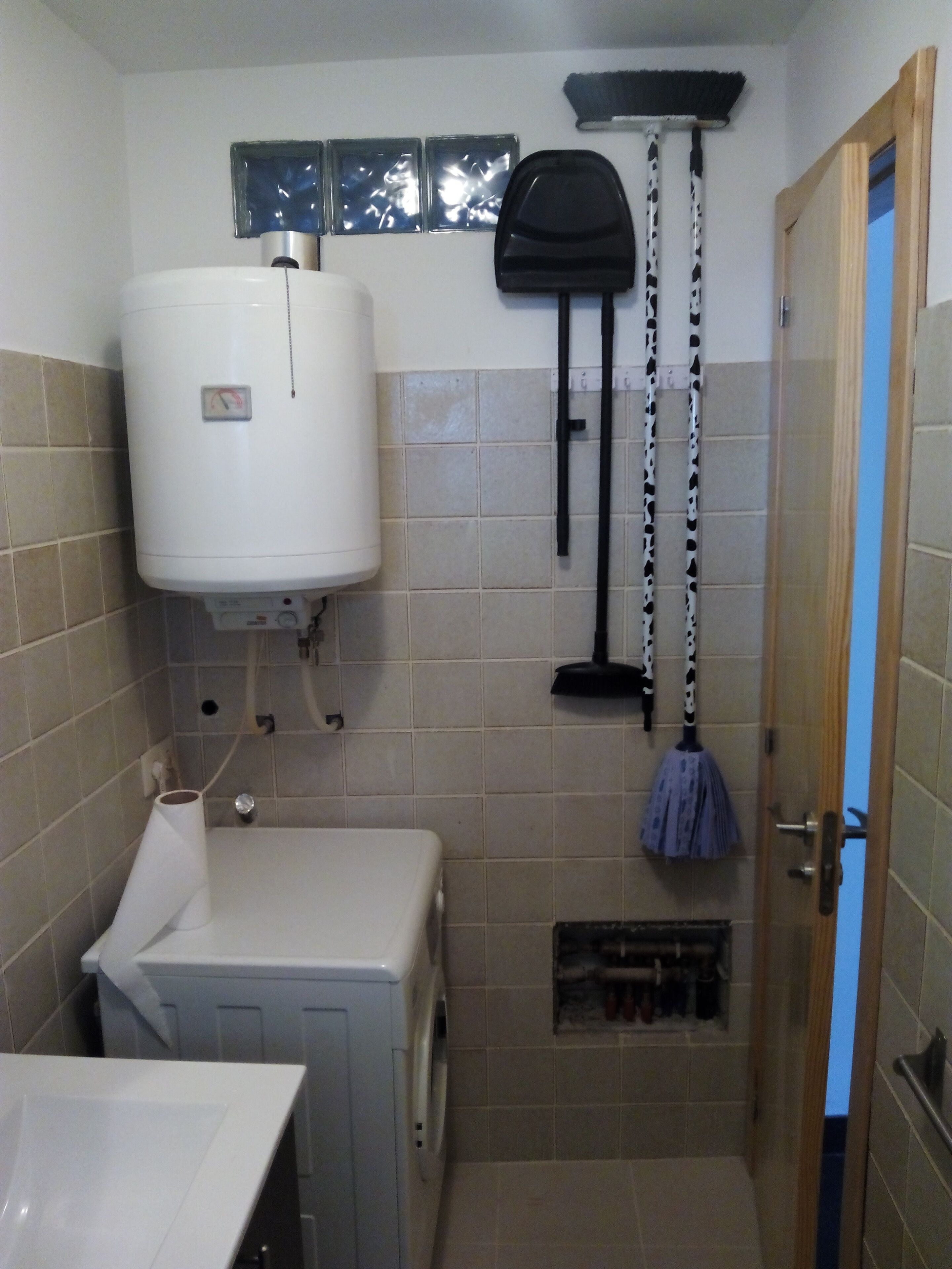 A small bathroom with a toilet, a sink, a white water heater, a mop, and a broom.