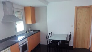Une cuisine compacte équipée d’une cuisinière, d’un four et d’un évier, ainsi qu’une table à manger avec des chaises et une porte en bois.