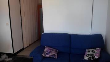 Un canapé bleu avec des coussins à motifs, dans une pièce dont le sol est carrelé et un des murs est blanc.
