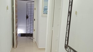 Un couloir doté d’un sol carrelé, une porte ornée d’un miroir décoratif, et une vue sur une autre pièce où se trouvent un lit et une fenêtre.