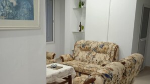 Un salon avec un ensemble de canapés à motifs floraux, une petite table recouverte d’une nappe blanche et un climatiseur fixé au mur.