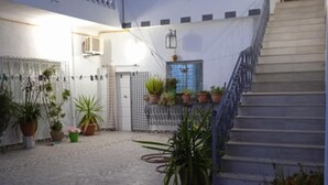 Une cour avec un sol carrelé, des plantes en pot, un escalier et un bâtiment blanc doté de balcons.