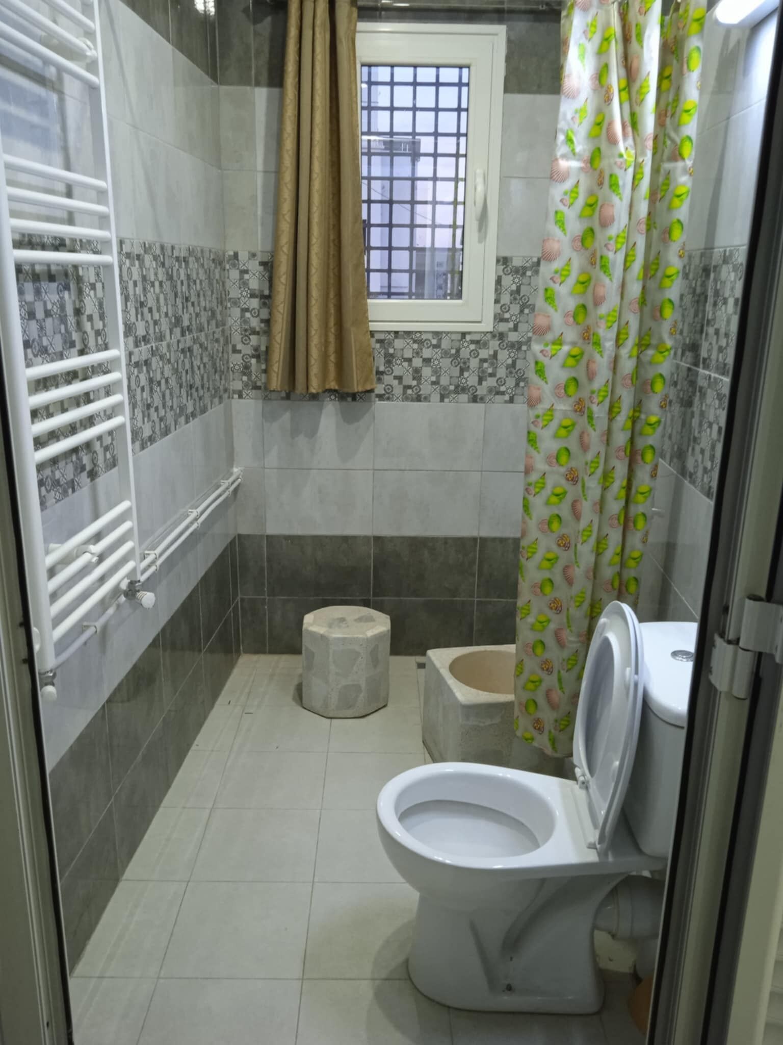 A small bathroom with a toilet, a shower curtain, and a window with bars.