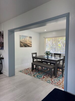 A dining area with a table, chairs, a bench, a patterned rug, and a painting on the wall.