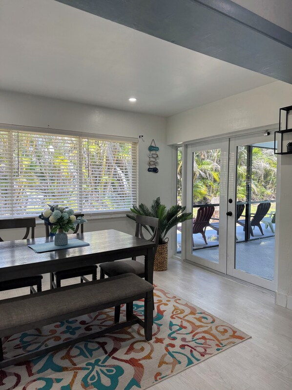A dining area with a table, chairs, a bench, a potted plant, and a view through a glass door to an outdoor patio.