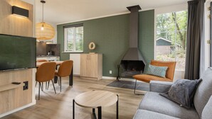 A modern living room with a fireplace, a dining area, and a kitchen. - Bungalow in Park De Peel - Car-free Retreat (Vlierden)