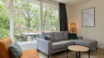 Relax in this stylish living room with a view of the lush outdoor area, featuring a comfortable sofa, armchair, and dining table.