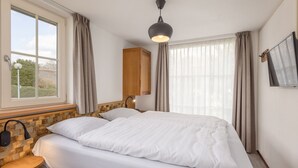 Una camera d'albergo con un letto grande, una testiera in legno, un comodino, una scrivania, una lampada, una TV montata a parete e una finestra con tende.