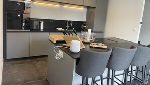 Eine moderne Küche mit grauen Schränken, einer schwarzen Arbeitsplatte und einer zentralen Kochinsel mit Barhocker.